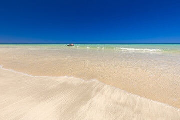Krajobraz morski, piaszczysta plaża i wybrzeże, żółty piasek, widok na lazurowe morze, niebieski kolor nieba, wyspa Djerba, Tunezja. Tapeta, egzotyczne tło © anettastar