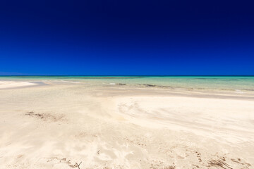 Krajobraz morski, piaszczysta plaża i wybrzeże, żółty piasek, widok na lazurowe morze, niebieski kolor nieba, wyspa Djerba, Tunezja. Tapeta, egzotyczne tło © anettastar