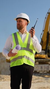 Foreman giving commands to employee in excavator using walkie talkie at construction site. Vertical video