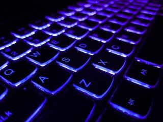 Laptop keyboard is glowing in the dark. Close up view of a modern laptop computer keyboard key with blue buttonss. Technology is a Sophisticated World. Modern blue iluminated backlit keyboard