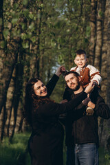 A mom and dad are walking together in a wooded area, holding a young son. The trio appear to be...