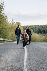 Portrait of a family walking in the middle of the road. The son runs ahead and enjoys the walk....