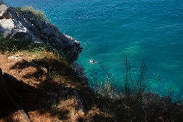 Aerial view of a person swimming in clear blue sea near rocky shore.