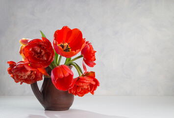 A bouquet of red tulips in a clay jug on a light background. Copy space