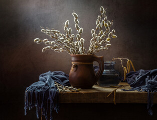 Still life with spring willow branches in a clay jug on a wooden table