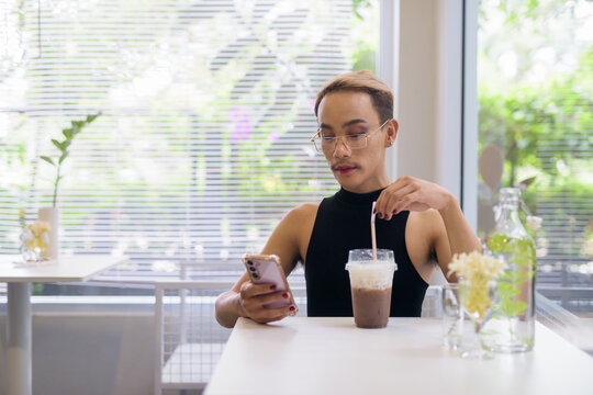 Beautiful Asian queer LGBT community supporter man using mobile phone in coffee shop