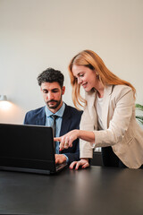 Vertical. One business woman and a businessman working together with a laptop on a job project. Two real coworkers planning using a computer. Teamwork of corporate employees on a brainstorming