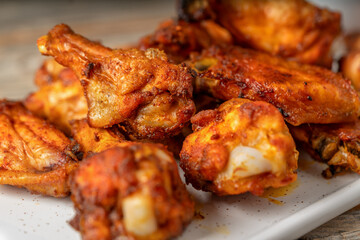Homemade baked or fried chicken wings in barbecue sauce on a white plate on a gray wooden table close-up closeup