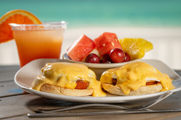 Eggs Benedict - two poached eggs on english muffin with ham topped with hollandaise and a side of fresh fruit.