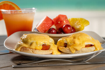 Eggs Benedict - two poached eggs on english muffin with ham topped with hollandaise and a side of fresh fruit.