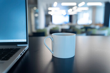 Close-up of a Coffee Cup Next to a Laptop with a Blurred Office Background
