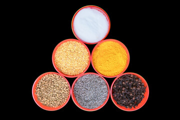 long view of red small bowls filled with salt, Fenugreek Seeds, turmeric powder, Mustard Seeds, Cumin Seeds, and Clove, Isolated on Black Background