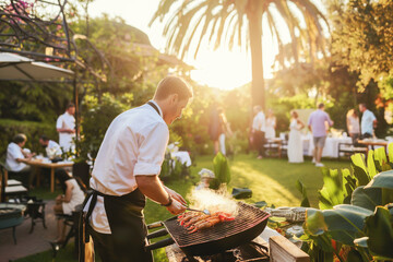 Caucasian male private chef grilling seafood at outdoor garden party. Sunlight filters through trees as guests enjoy festive atmosphere