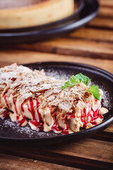 Puff pastry layered napoleon cake. Dessert with juicy vanilla cream and cherry raspberry filling, crumble served on a plate on table in restaurant cafe. Restaurant dish. Specialty coffee aesthetics