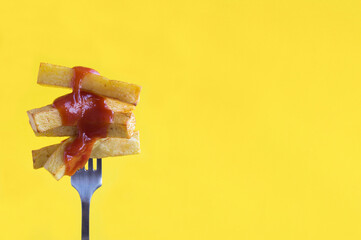 French fries with ketchup chopped on a fork on the yellow background. Close-up. Copy space.