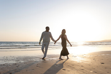 A couple is walking on the beach holding hands