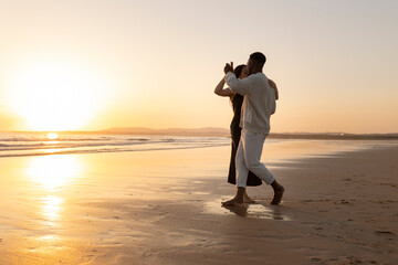 A couple is dancing on the beach at sunset