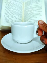 Black male hand holding taking cup of coffee and a open book on the wooden table