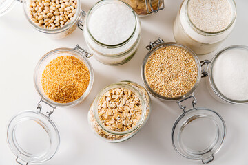 food storage, culinary and eating concept - close up of jars with different cereals, salt, sugar and beans on white background, top view