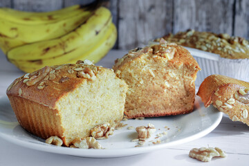 Banana pancake with granola and walnut on top, on a white plate and bananas out of focus in the background. Homemade pastry concept.