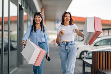 Two trendy female buyers having fun at shopping center at shopping spree