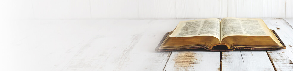 Fototapeta premium Open holy bible on a white wooden surface. With extra wide copy space to add text. Holy scriptures. Ideal for blogs, presentations, religious meetings, Prayer groups and much more. Panoramic banner.