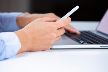 Side view shot of a woman's hands using smart phone and laptop computer 