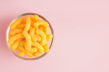 Glass bowl with tasty salty corn sticks on pink background