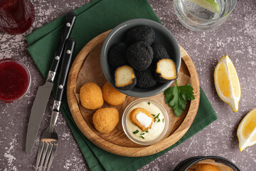 Wooden board with different delicious fried mozzarella balls, sour cream and glass of water on grunge background
