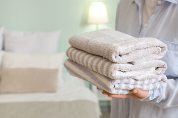 Woman holding stack of clean soft towels in bedroom