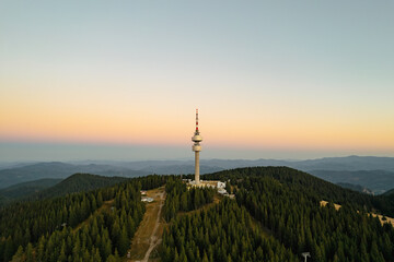 Aerial view tower structure high in mountains aerial view drone forward, dense pine forest at sunrise in summer morning on blue sky. Panorama post-dawn blue sky high in mountains. Nature Bulgaria