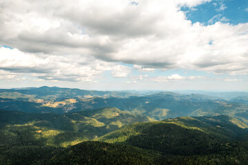 Fototapeta premium Green coniferous forest and grass meadows top view aerial view. Beautiful mountain range against blue sky on sunny