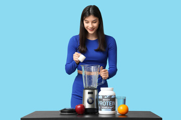 Beautiful sporty woman making protein shake on color background