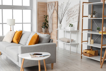 Interior of stylish living room with sofa, shelf units and willow branches in vase