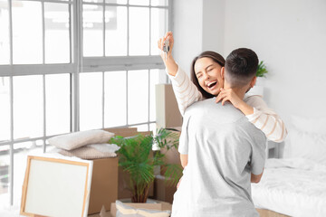 Young woman with keys hugging her husband in bedroom on moving day