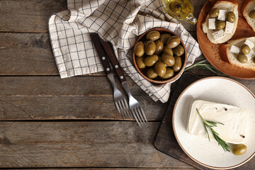 Plate with tasty feta cheese, olive, rosemary and peppercorn on wooden background