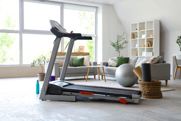 Modern treadmill with sports equipment in living room interior