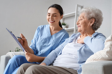 Physical therapist with clipboard and senior woman sitting on sofa at home