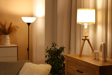 Glowing lamp on chest of drawers, statuette and houseplant in stylish living room