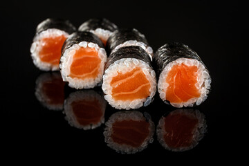 Sushi roll with salmon, on a black mirror