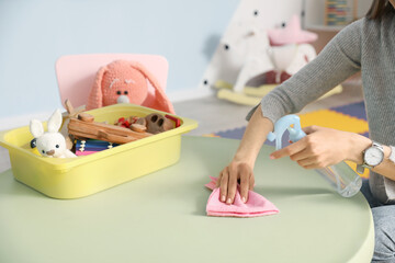 Female nursery teacher disinfecting table in kindergarten, closeup
