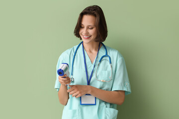Beautiful female doctor with infrared thermometer and badge on green background