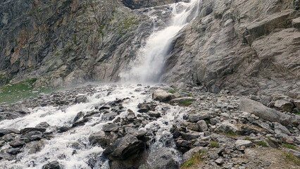 Obraz premium A stunning waterfall cascades down a rocky cliffside, creating a powerful and dynamic flow of water over rugged terrain. The scene is set in a mountainous area with lush greenery.