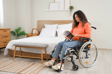 Young African-American woman in wheelchair reading magazine at home