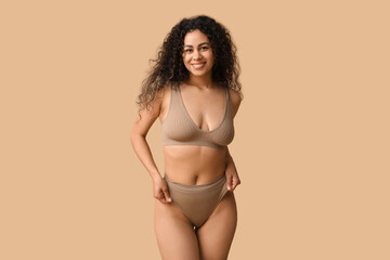 Beautiful young happy African-American woman in underwear on beige background