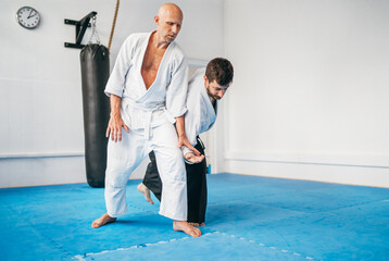 Two men are practicing Aikido in dojo wearing traditional white Kimono and Hakama .One man executes...
