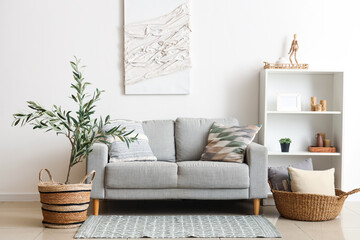 Interior of beautiful living room with grey sofa, shelving unit and olive tree