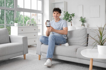 Diabetic young man with glucose sensor and mobile phone measuring blood sugar level on sofa at home