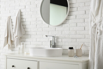 Ceramic sink, mirror and chest of drawers near white brick wall in bathroom
