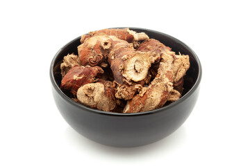 Close-up of Dry Organic Kulanjan (Alpinia galanga) roots, in black ceramic bowl. Isolated on a white background.
